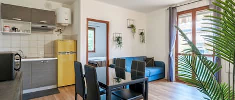 Un espacio habitable compacto con kitchenette, comedor, sofá y un amplio ventanal con cortinas.