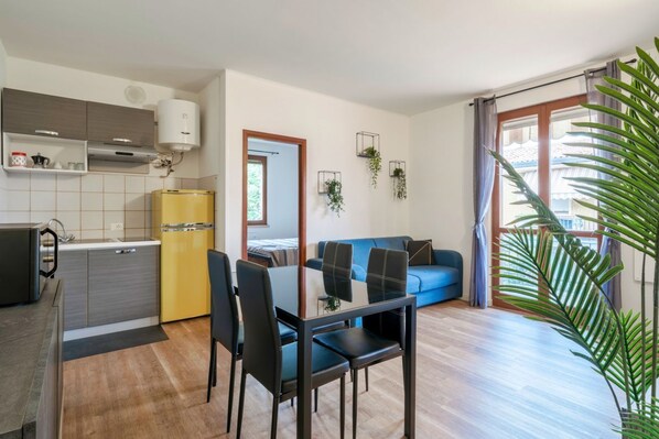 A compact living space with a kitchenette, a dining area, a sofa, and a large window with curtains.