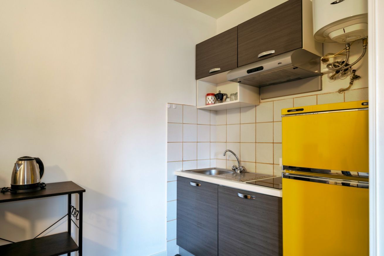 A compact kitchen with a yellow refrigerator, a built-in oven, and a coffee maker on a small table.
