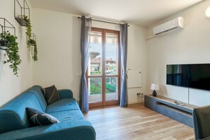 A modern living room with a blue sofa, a flat-screen TV, and a sliding glass door leading to a balcony. - Moretto 11. with pool and WiFi (Sirmione)