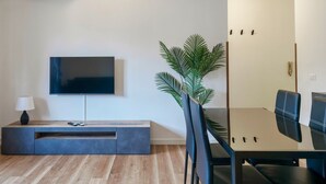 A modern living room with a flat-screen TV mounted on the wall, a dark wooden entertainment unit, a dining table with black chairs, and a potted plant. - Moretto 11. with pool and WiFi (Sirmione)