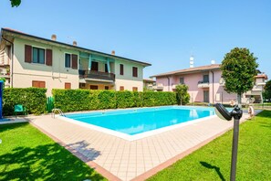 A swimming pool surrounded by a well-maintained lawn and a row of residential buildings. - Moretto 11. with pool and WiFi (Sirmione)
