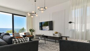Un salón moderno con un televisor grande, asientos cómodos y vistas al mar.