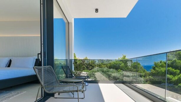 Un dormitorio moderno con un gran ventanal, una cama y una zona de estar con vistas al mar.