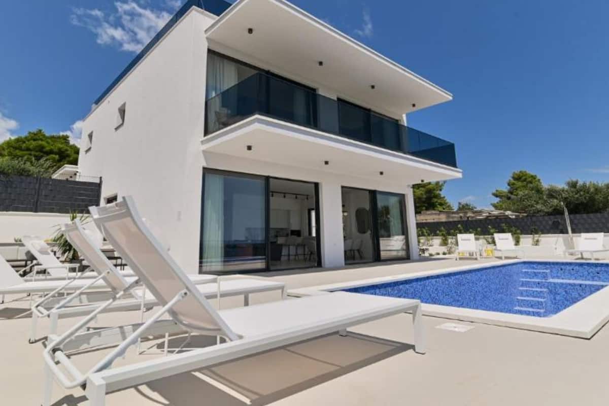 A modern two-story house with a swimming pool, white exterior, and large glass windows.