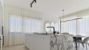 Una cocina moderna con una isla de mármol, armarios blancos y un comedor con mesa y sillas.