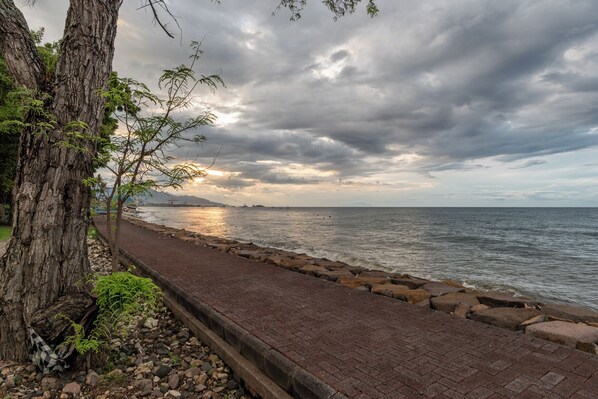 A coastal walkway with a brick path, rocky shoreline, and a tree on the left. - Villa Burung (Seririt)