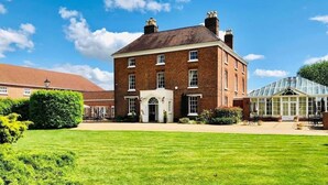 A large brick building with a central entrance, surrounded by a well-maintained lawn and a greenhouse structure. - Hadley Park House Hotel (Telford)