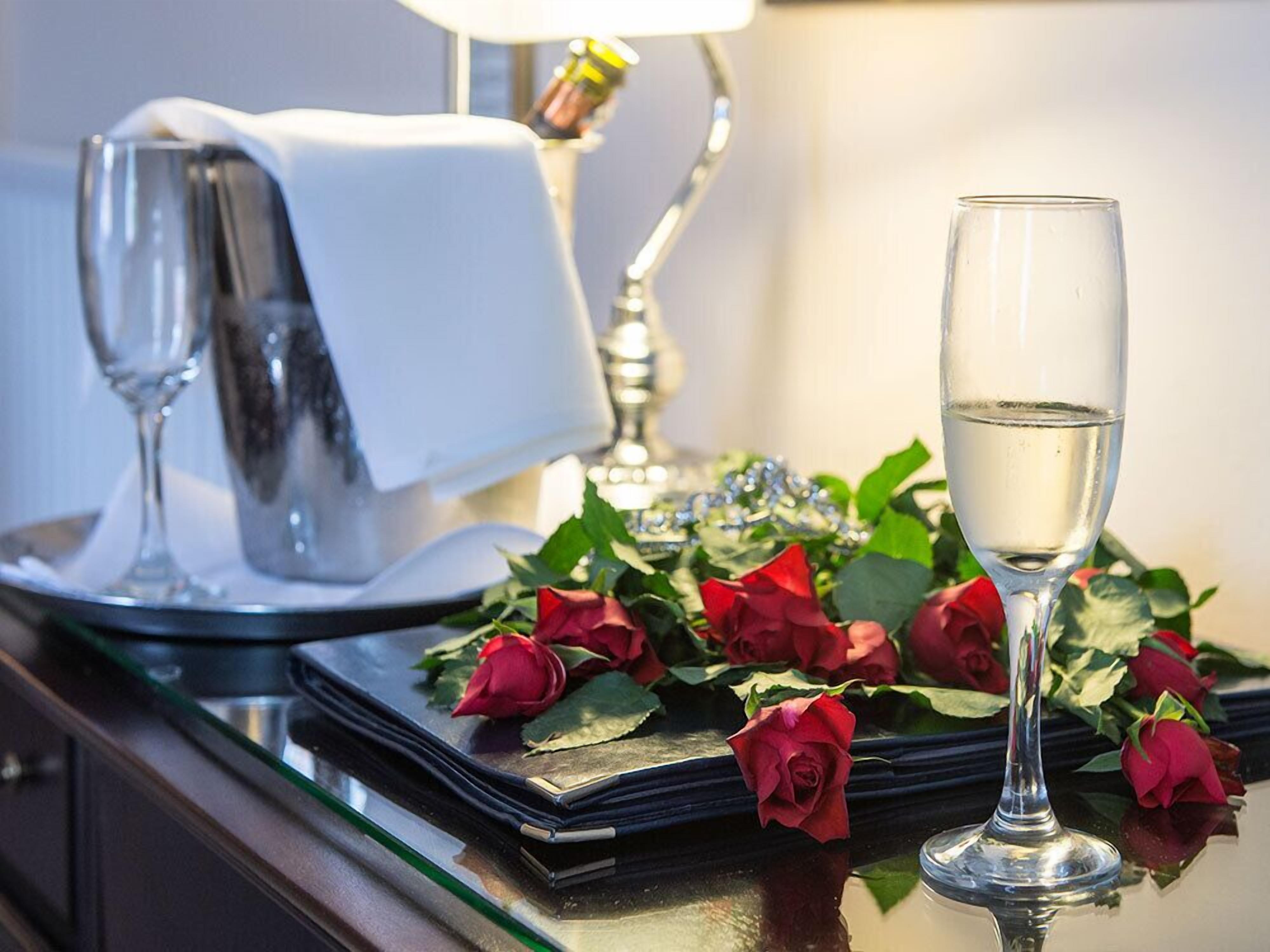 A table with a glass of water, a folded napkin, a silver pitcher, and a bouquet of red roses.