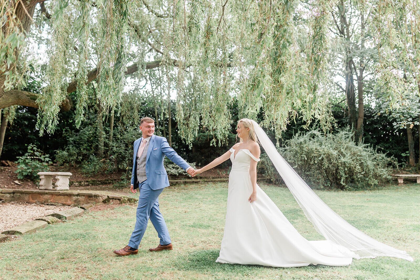 A couple holding hands in a garden with a tree overhead.