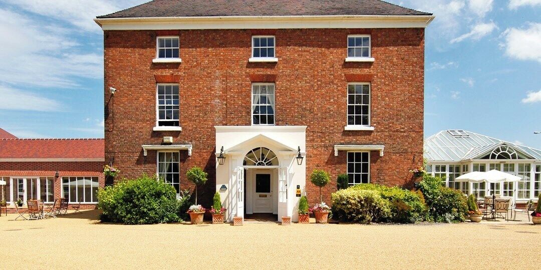 A large brick building with a symmetrical facade, a central entrance with a white archway, and a conservatory to the right.