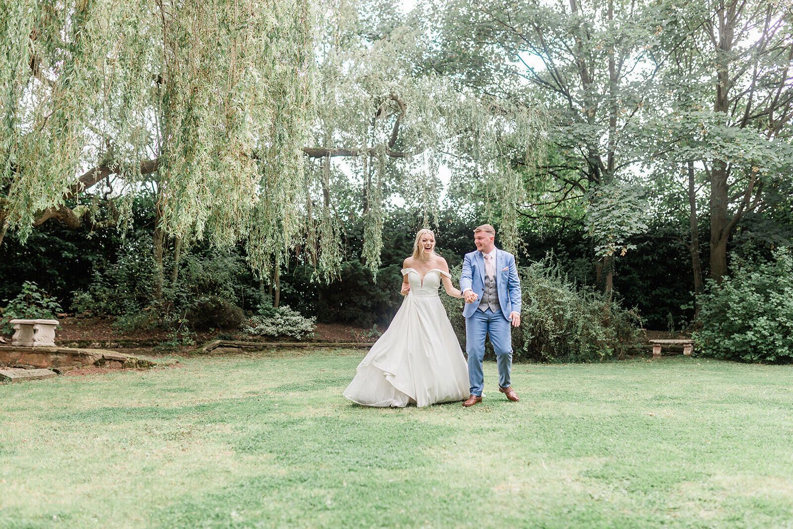 A couple in a garden setting with a stone bench and lush greenery in the background.