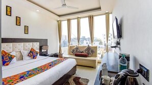A hotel room with a large bed, a sofa, a desk with a computer, and a window with curtains. - Hotel City Pride (Haridwar)