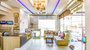 A modern reception area with a counter, seating, and a large window providing a view of the outside. - Hotel City Pride (Haridwar)
