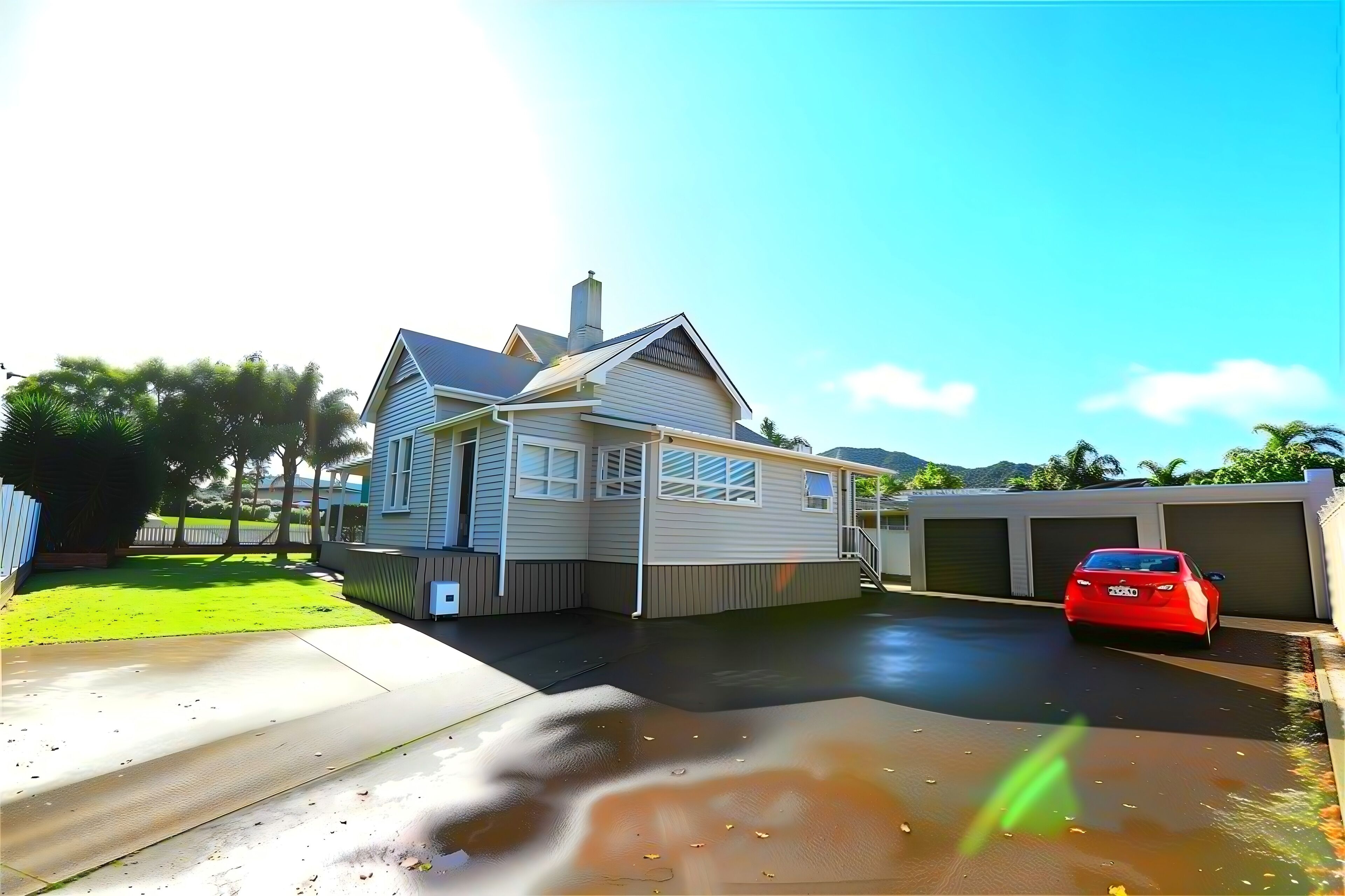 Een woonhuis met een garage, oprit en rode auto geparkeerd in de garage.