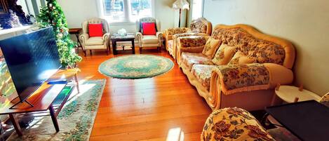 A living room with a wooden floor, a sofa set, a television, and a Christmas tree.