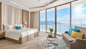 A modern hotel room with a large bed, a sofa, a coffee table, and a view of the sea.