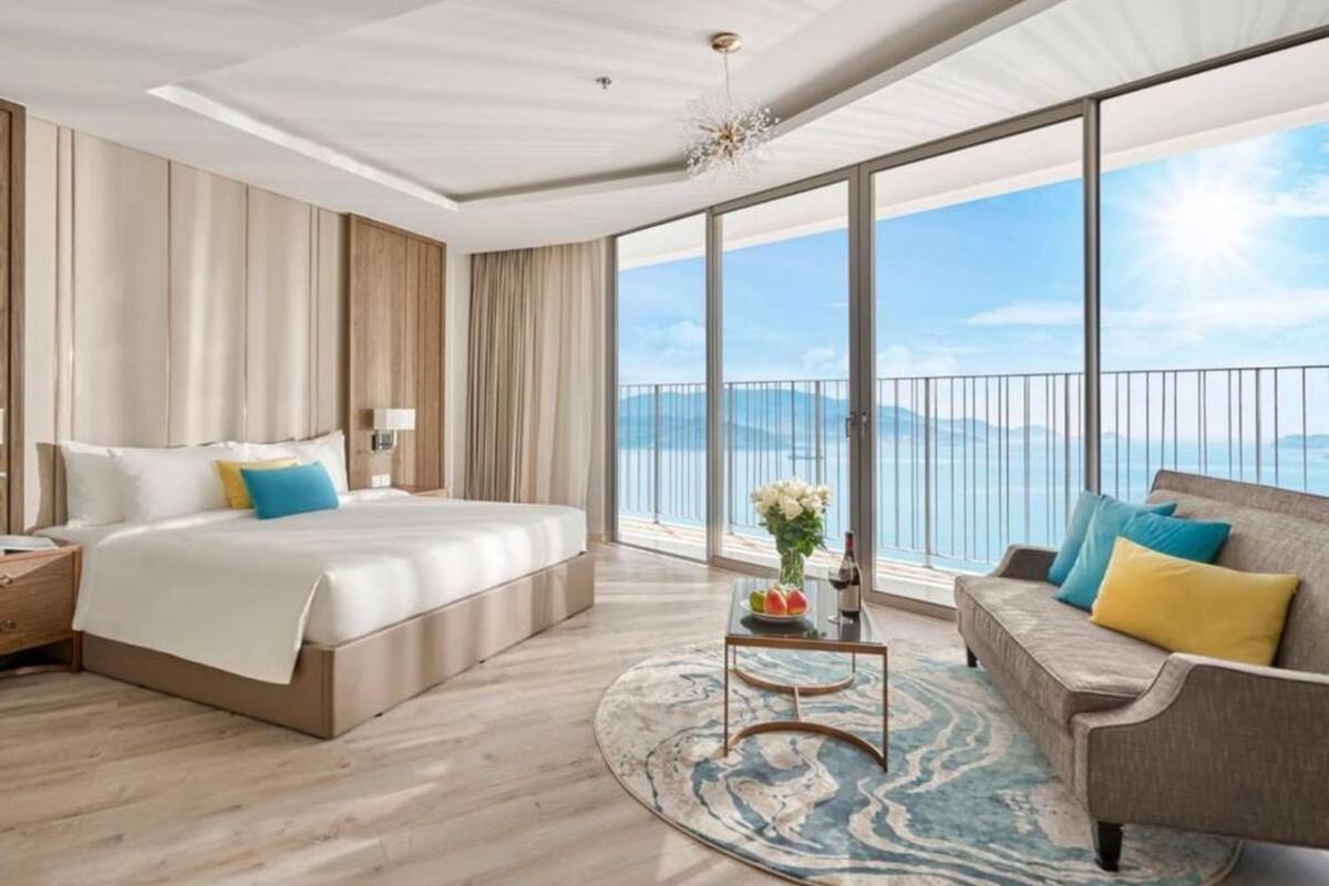 A modern hotel room with a large bed, a sofa, a coffee table, and a view of the sea.