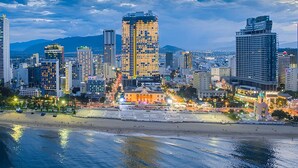 A coastal cityscape with high-rise buildings, a beach, and mountains in the background.