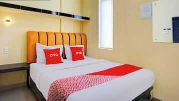 Una habitación de hotel con una cama, cabecera, mesita de noche y ventana.