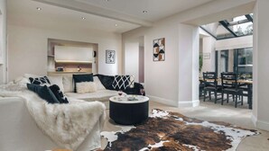 A modern living room with a white sofa, a round coffee table, and a cowhide rug. There is a dining area visible through an open door. - Rosemount Lakes Townhouse with Hot Tub | Ridgestone (Windermere)