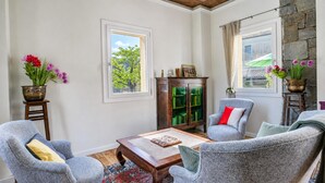 Ein Wohnzimmer mit Couchtisch aus Holz, zwei grauen Sesseln, einer Kommode und einem Fenster mit Vorhängen.