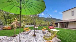 Eine Terrasse mit Steinfliesen, Gartenmöbeln und einem grünen Sonnenschirm.