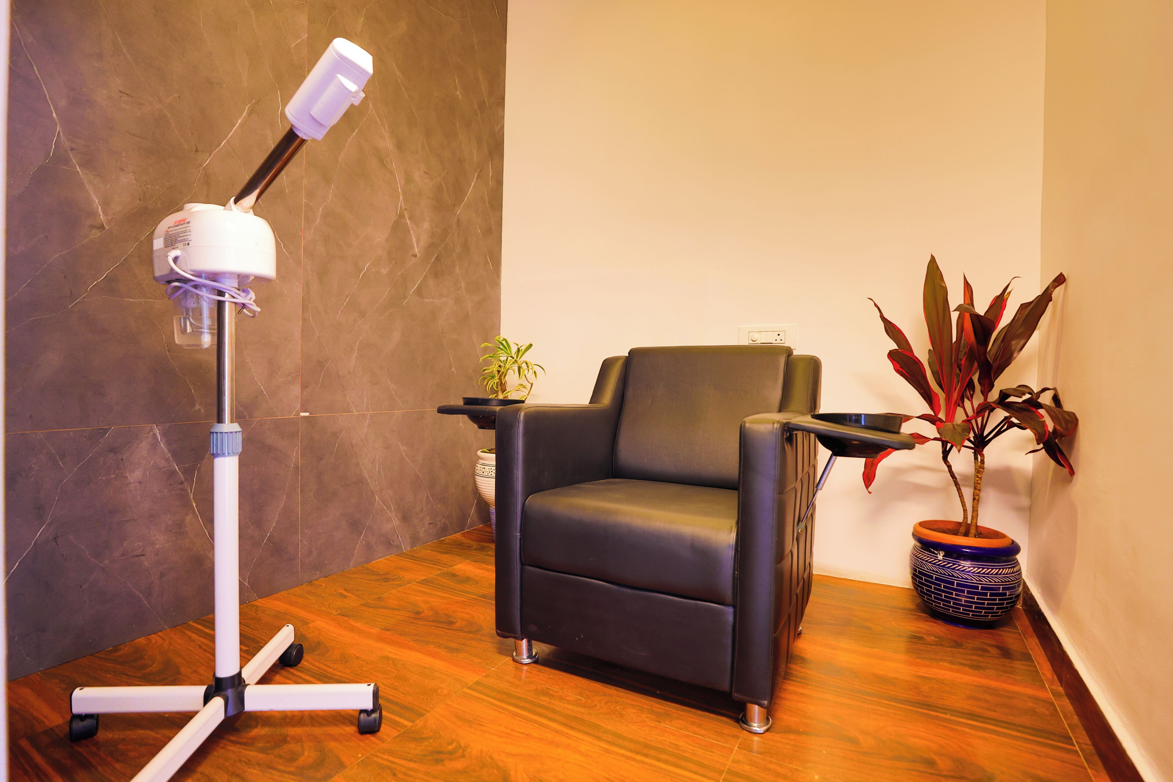 A room with a black leather chair, a white desk lamp, and two potted plants.
