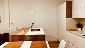 Een moderne keuken met een houten eettafel, witte stoelen en een ingebouwd spoelgedeelte.