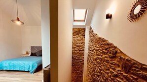 Een slaapkamer met een blauw beddegoed, een hanglamp en een dakraam.