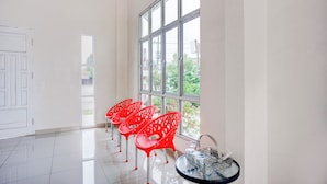 A room with a large window, white walls, and a tiled floor. There are four red chairs and a small table with a glass container.