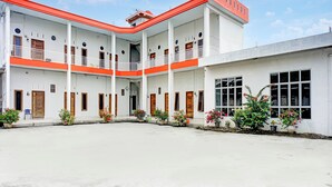 A multi-story building with a white facade and red accents, featuring balconies and potted plants.