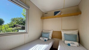 Une petite pièce, de taille modeste, avec deux lits simples, une étagère en bois au-dessus et une fenêtre donnant sur la verdure.