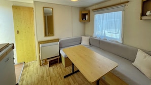 Un intérieur de camping-car compact comprenant un coin cuisine, un canapé, une table et une fenêtre avec des rideaux.