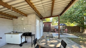 Un patio couvert comprenant un coin cuisine équipé d’un évier, d’un petit réfrigérateur et d’une table avec des chaises.