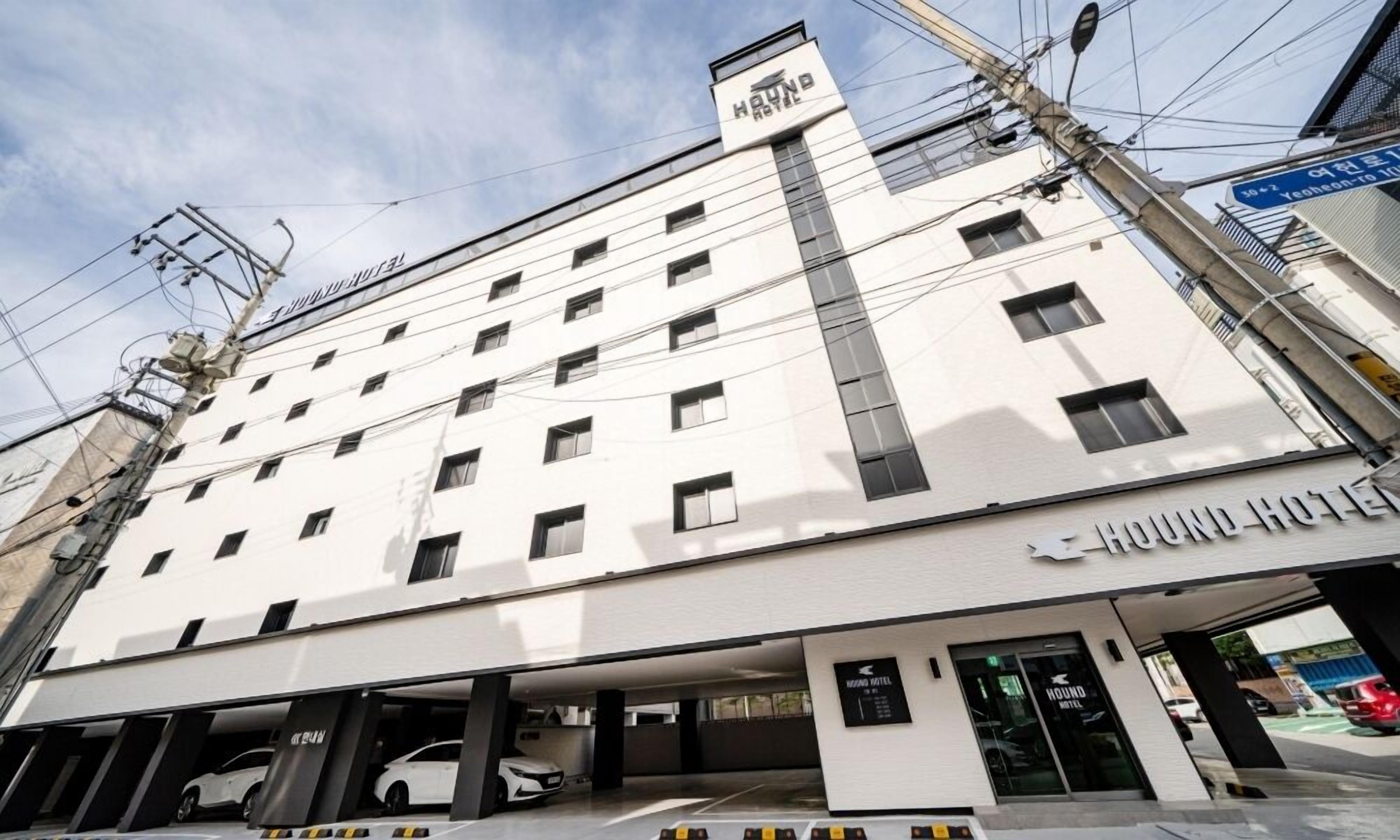 A multi-story building with a sign for 'HOUND HOTEL' on the ground floor. There are multiple windows on each floor, and a parking garage is visible below.