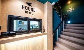 A reception desk with a sign for HOUND HOTEL, a key box, and a staircase.