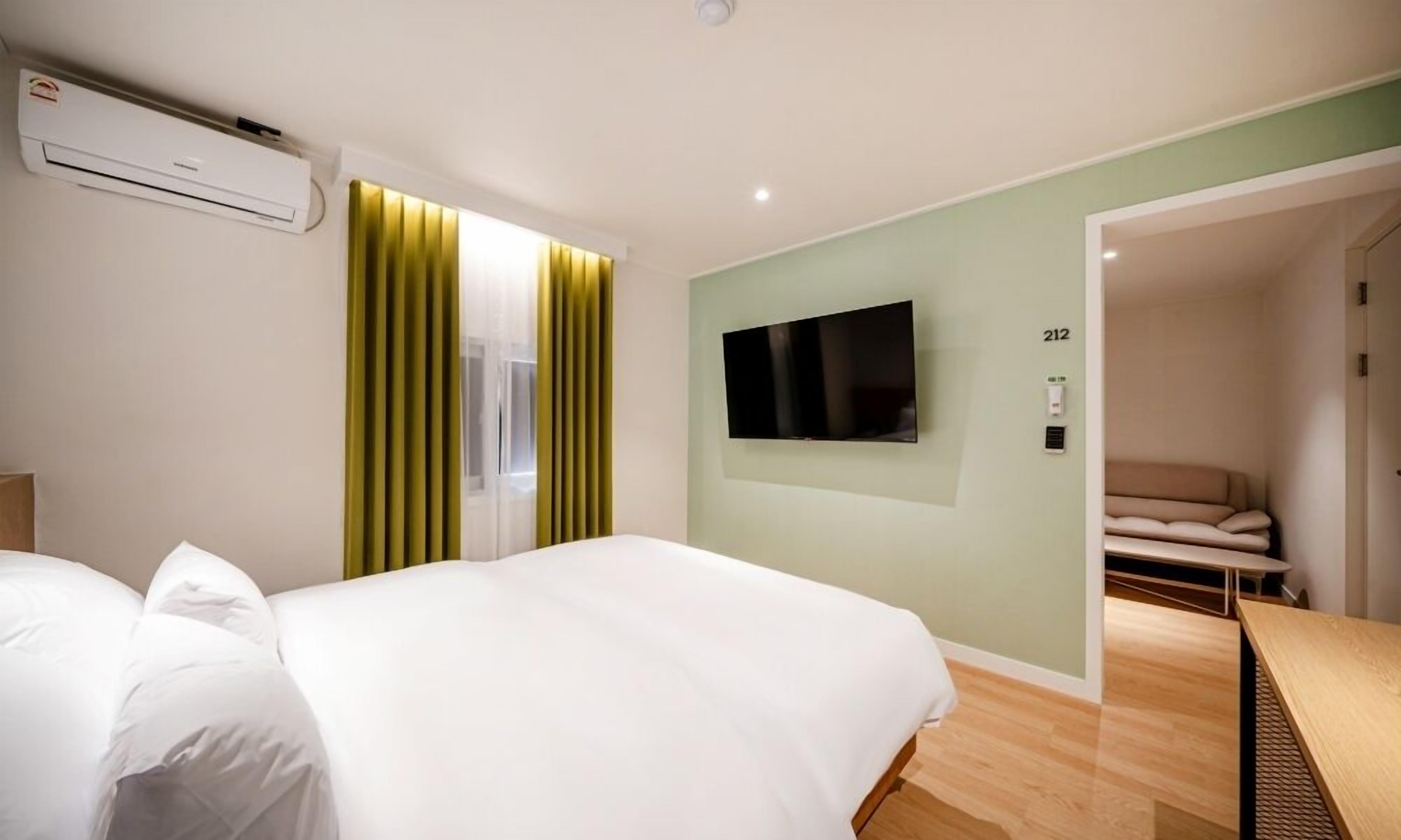A hotel room with a bed, a TV mounted on the wall, and a door leading to a seating area.