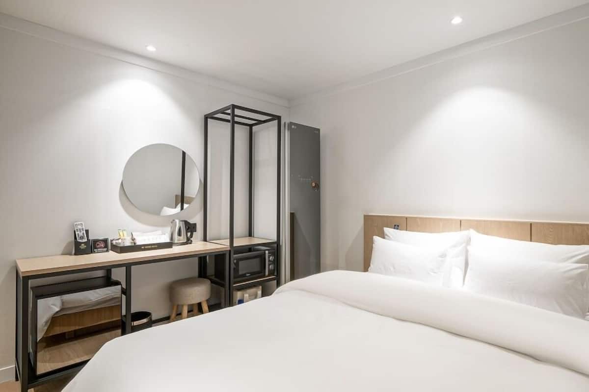 Ein Hotelzimmer mit Bett, Schreibtisch, Stuhl, Spiegel und Kleiderschrank.