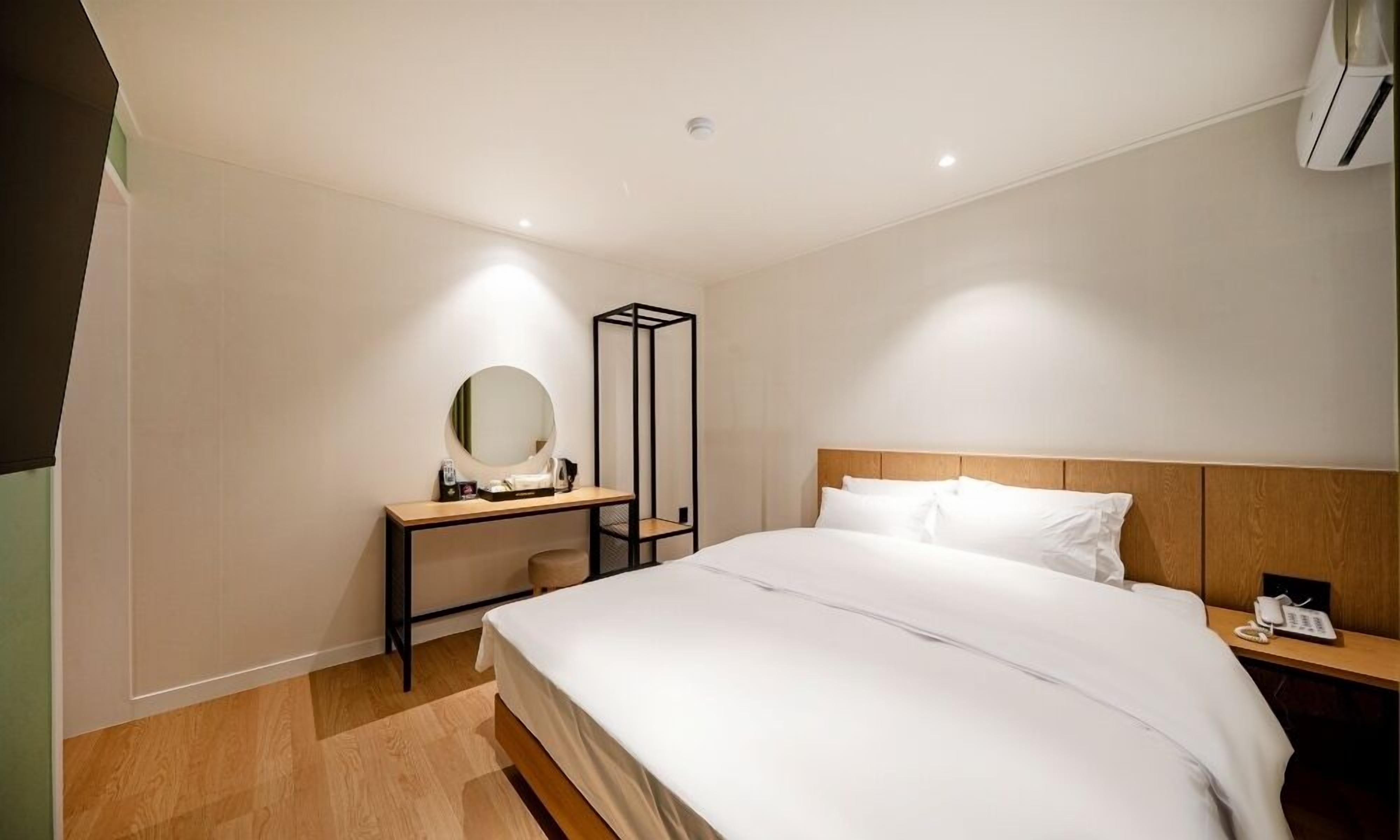 A hotel room with a bed, bedside table, a mirror, and a small desk with a chair.