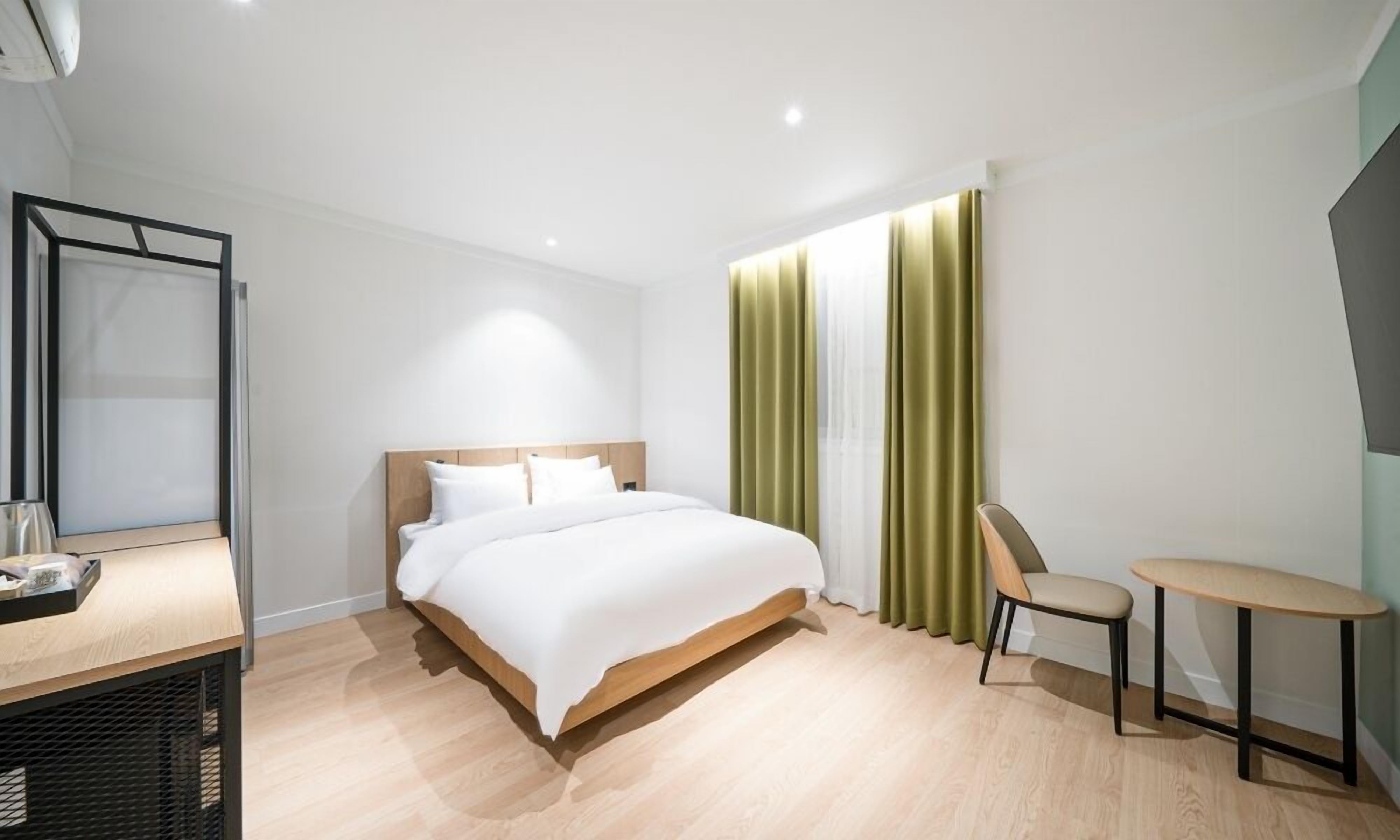 Una habitación de hotel moderna con una cama de madera, un escritorio, una silla y una mesita.