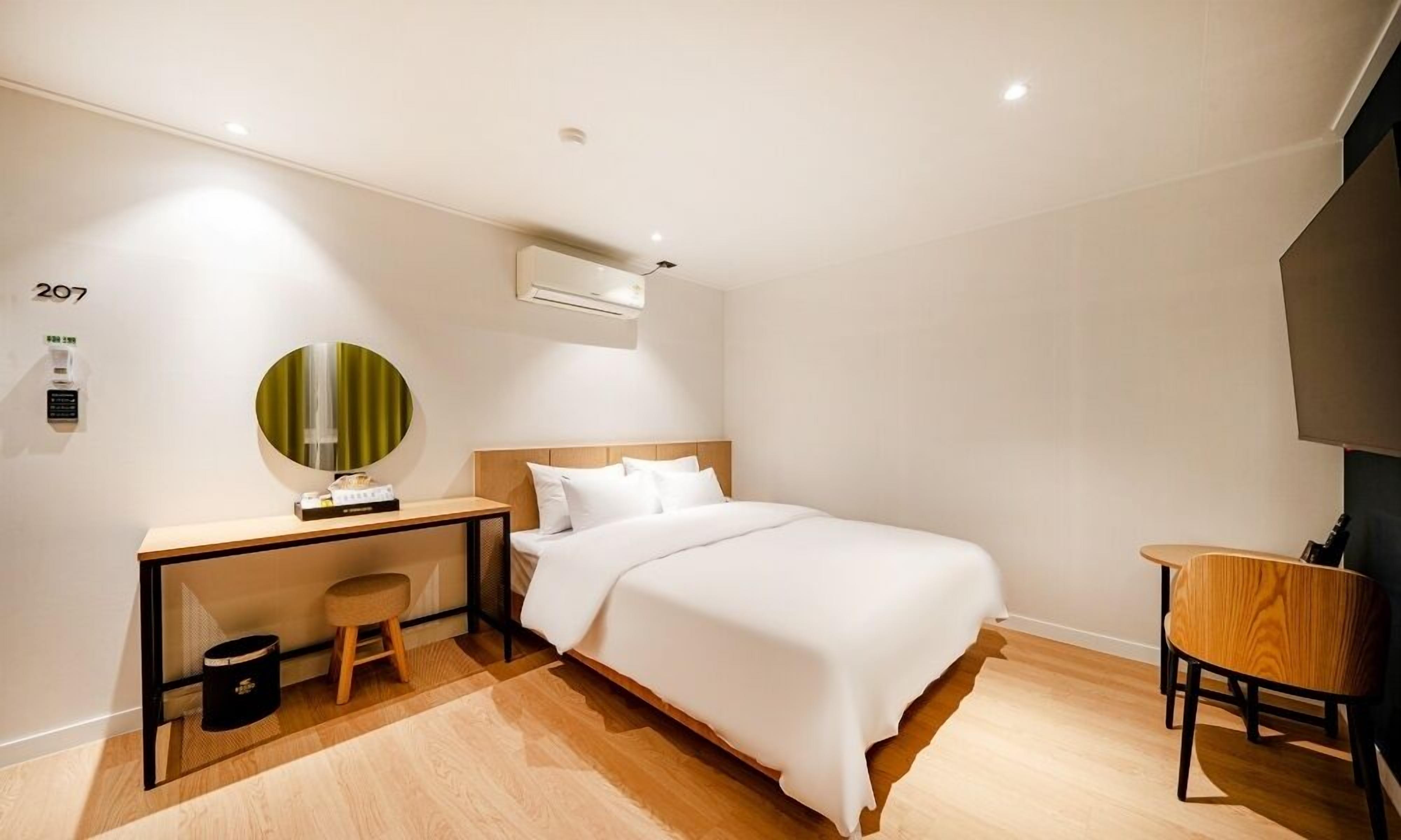 Una habitación de hotel moderna con cama, escritorio, silla y un taburete pequeño.