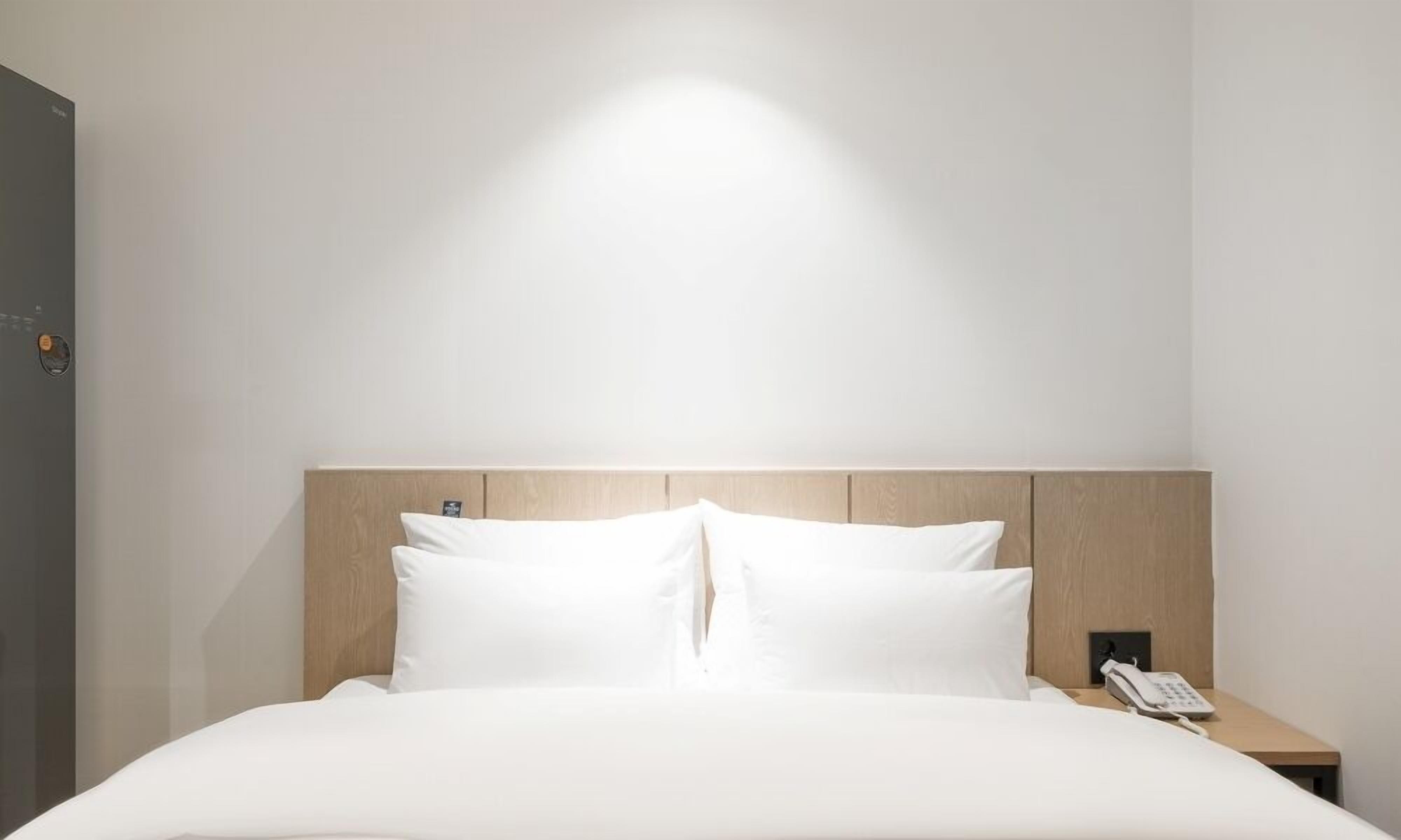Habitación de hotel con cama, cabecera de madera, mesita de noche con teléfono y lámpara de pared.