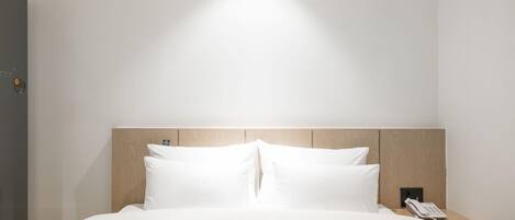 A hotel room with a bed, a wooden headboard, a bedside table with a phone, and a wall-mounted light.