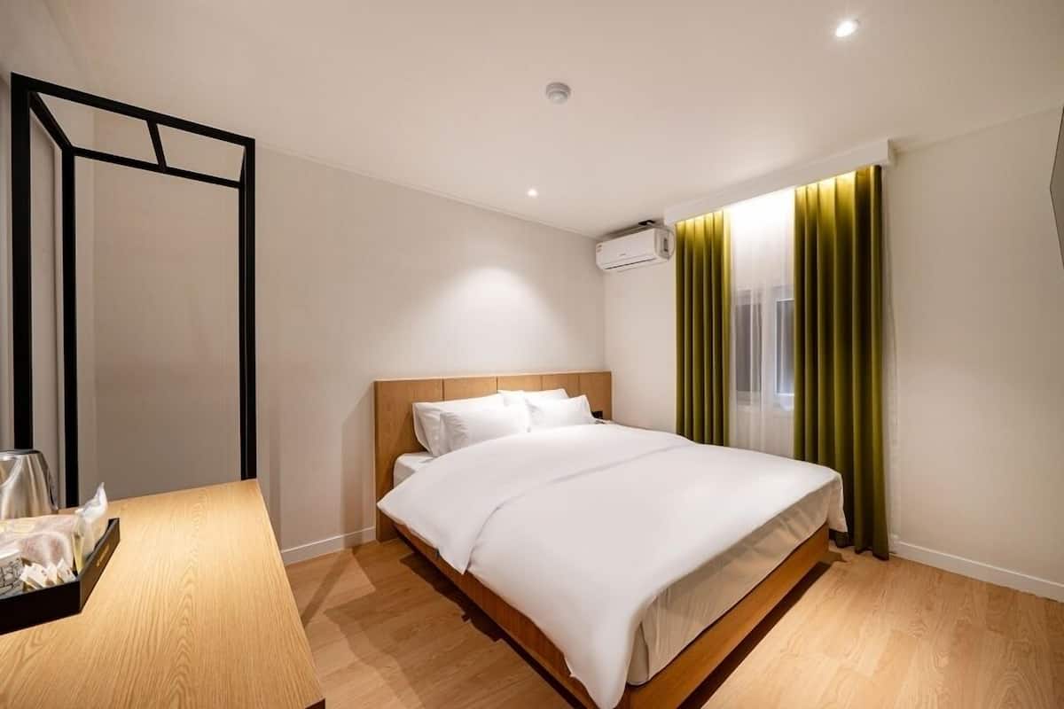 Ein Hotelzimmer mit einem Holzbett, einem Nachttisch, einem Spiegel und einem Fenster mit Vorhängen.