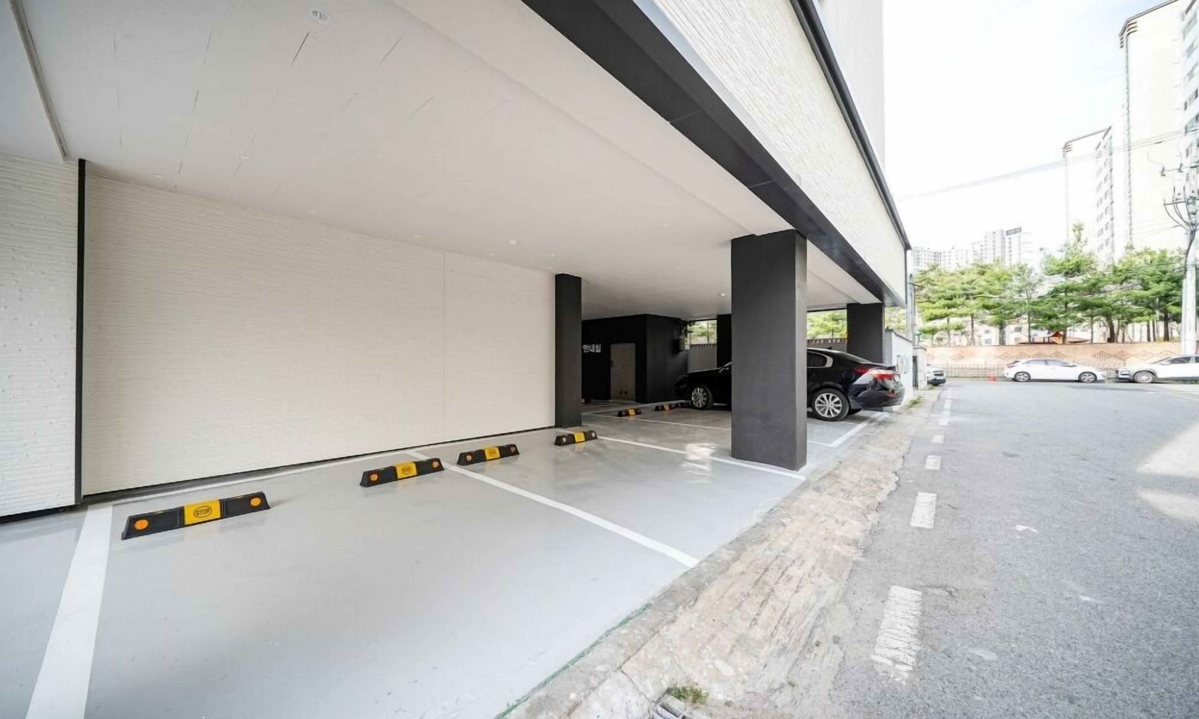 An empty parking garage with concrete floors and columns, a few parked cars, and a building with a white facade.
