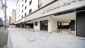 En moderne bygning med et skilt, der siger 'HOUND HOTEL', overdækket parkering og en ren, asfalteret sti.
