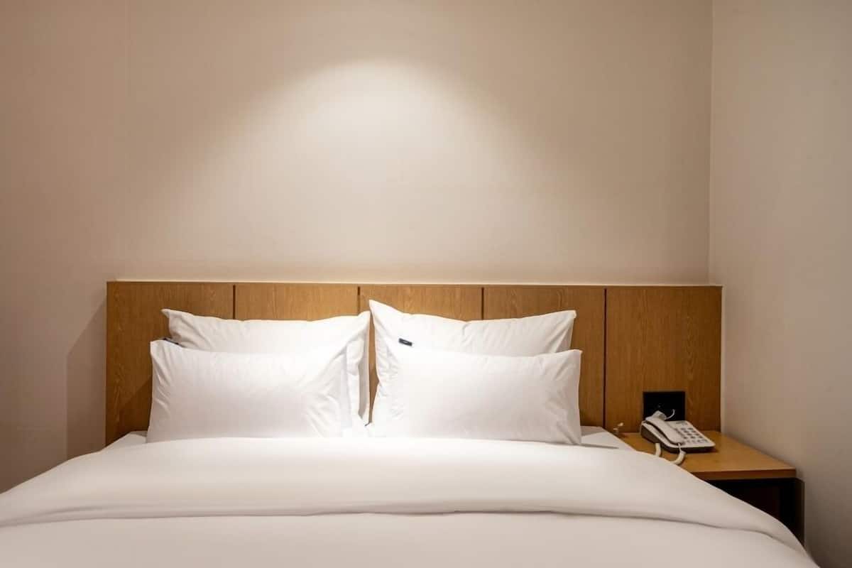 Ein Hotelzimmer mit hölzernem Kopfteil, einem Bett mit weißen Leinentüchern und einem Nachttischtelefon.