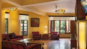 A spacious living room with a red sofa, a wooden coffee table, and a ceiling fan. - Norling House (Dharamshala)