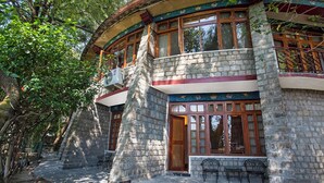 A stone building with a balcony, a wooden door, and outdoor seating. - Norling House (Dharamshala)